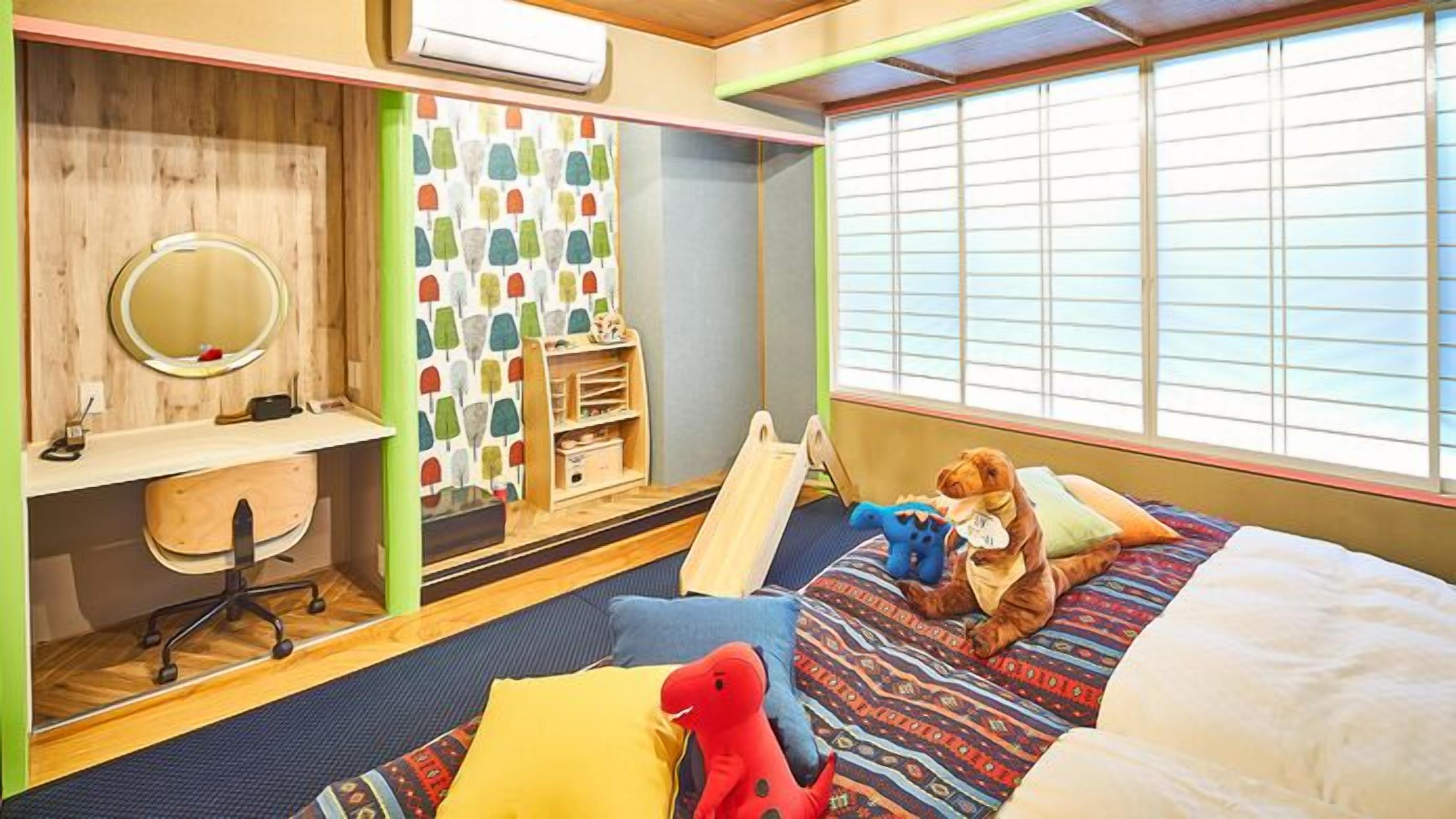 Ein Schlafzimmer mit einem Bett, einem Schreibtisch mit Stuhl, einem Fenster mit Jalousien und einem Regal mit Spielzeug.