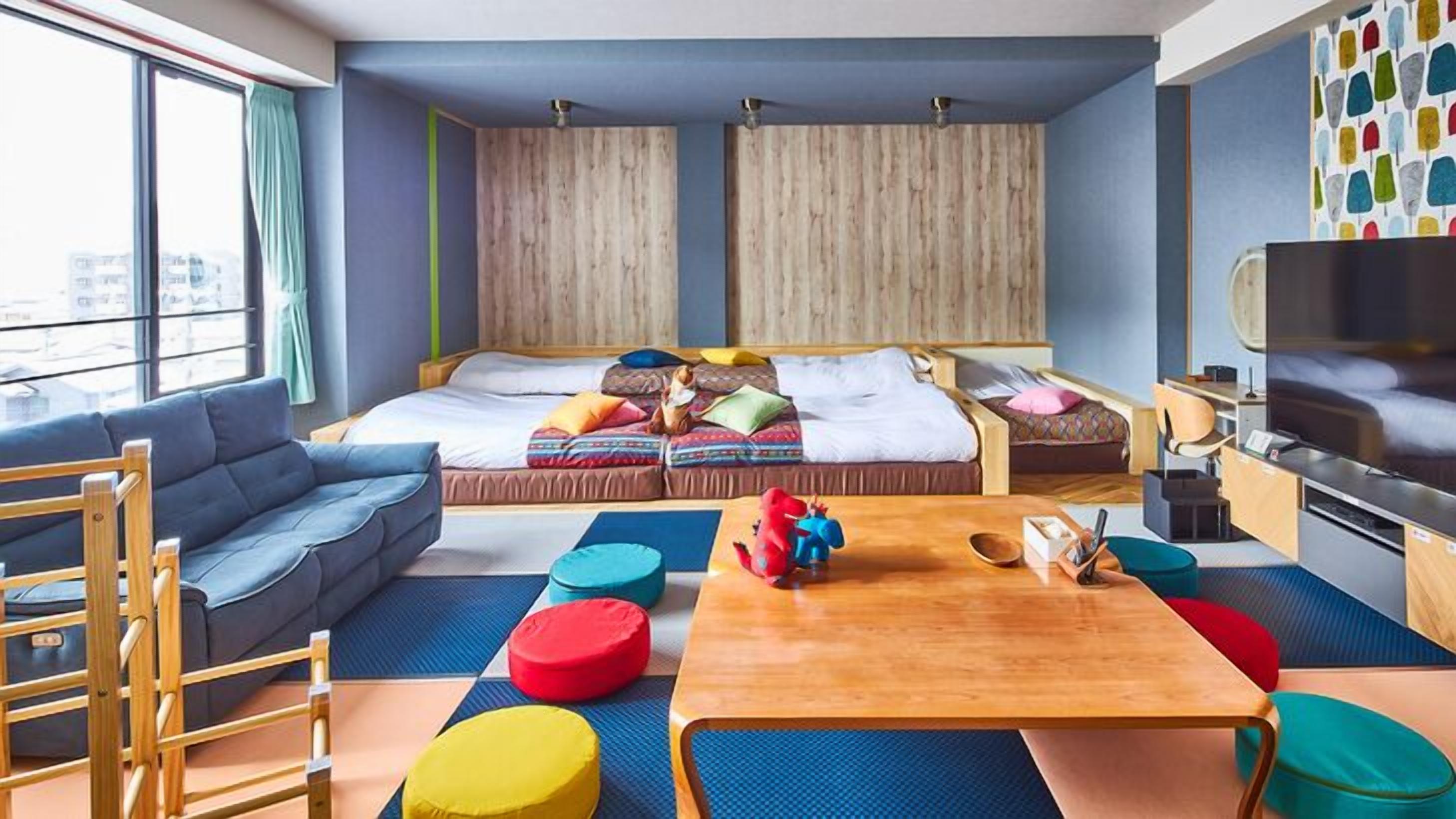 Ein modernes Zimmer mit einer Couch, zwei Betten, einem Fernseher und farbenfrohen Kissen.