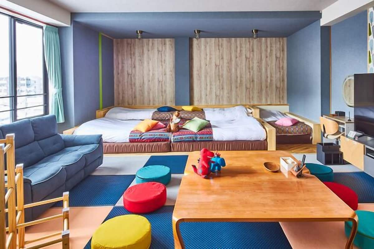 Ein modernes Zimmer mit einer Couch, zwei Betten, einem Fernseher und farbenfrohen Kissen.