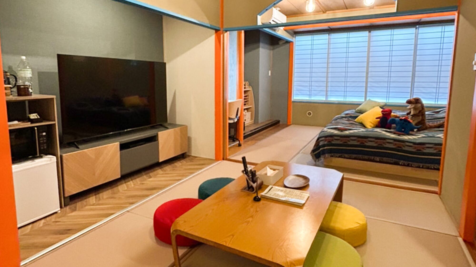 Ein kleines Zimmer mit Fernseher, einer kleinen Küchenzeile, einem Bett mit Spielzeug und einer Schiebetür zum Balkon.
