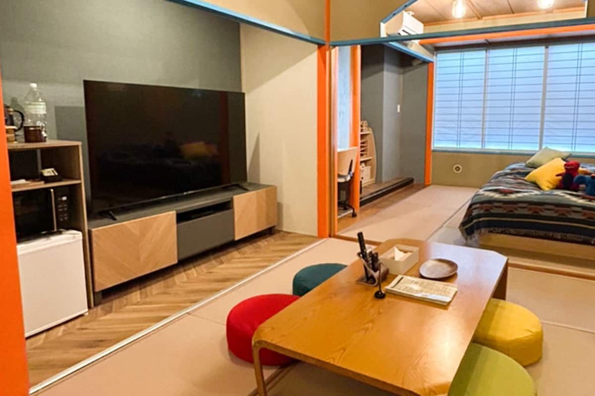 Ein kleines Zimmer mit Fernseher, einer kleinen Küchenzeile, einem Bett mit Spielzeug und einer Schiebetür zum Balkon.