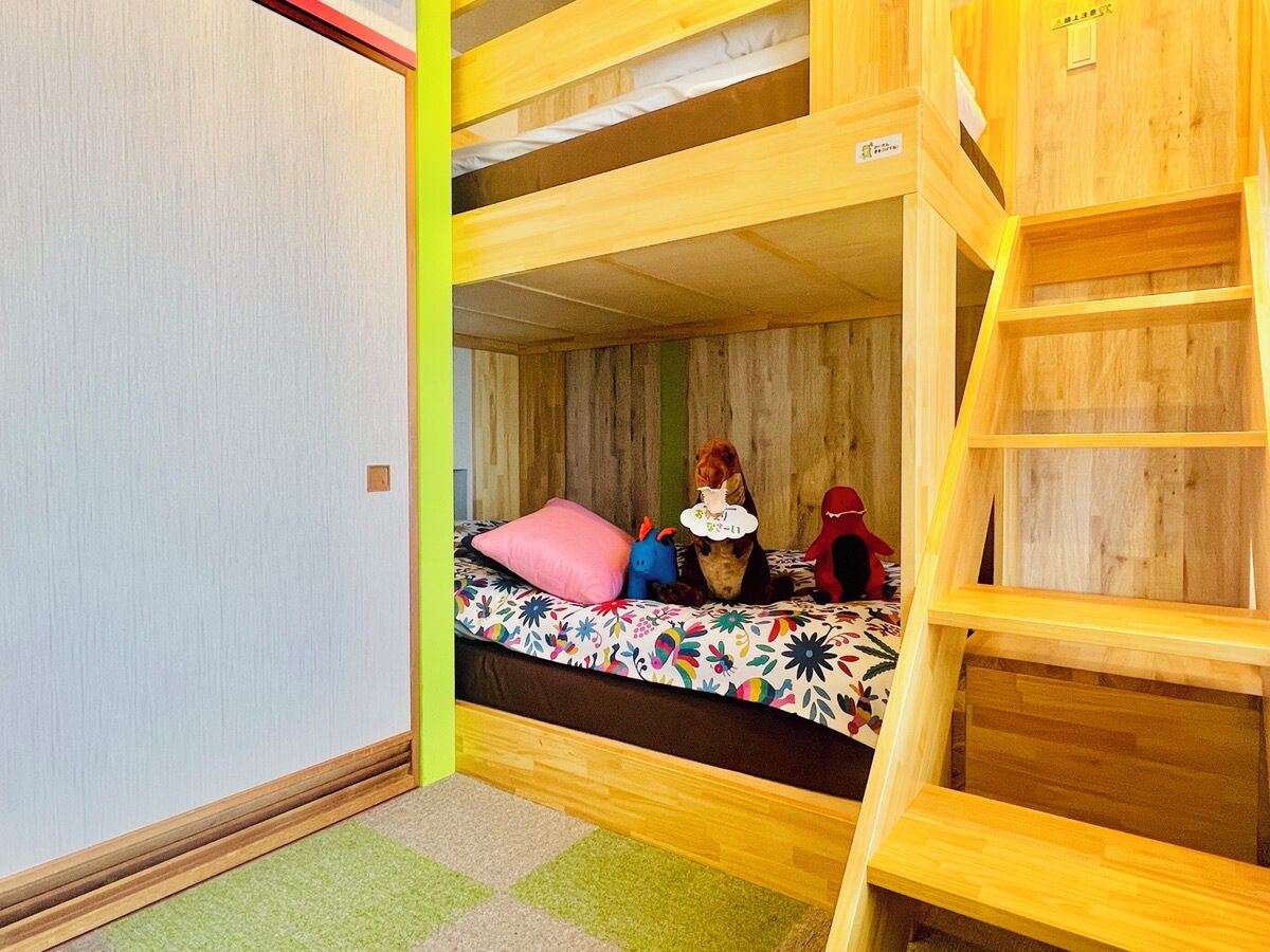 Ein Schlafraum mit Etagenbett, einer Holzleiter, einer bunten Bettdecke und einem grünen Teppich.