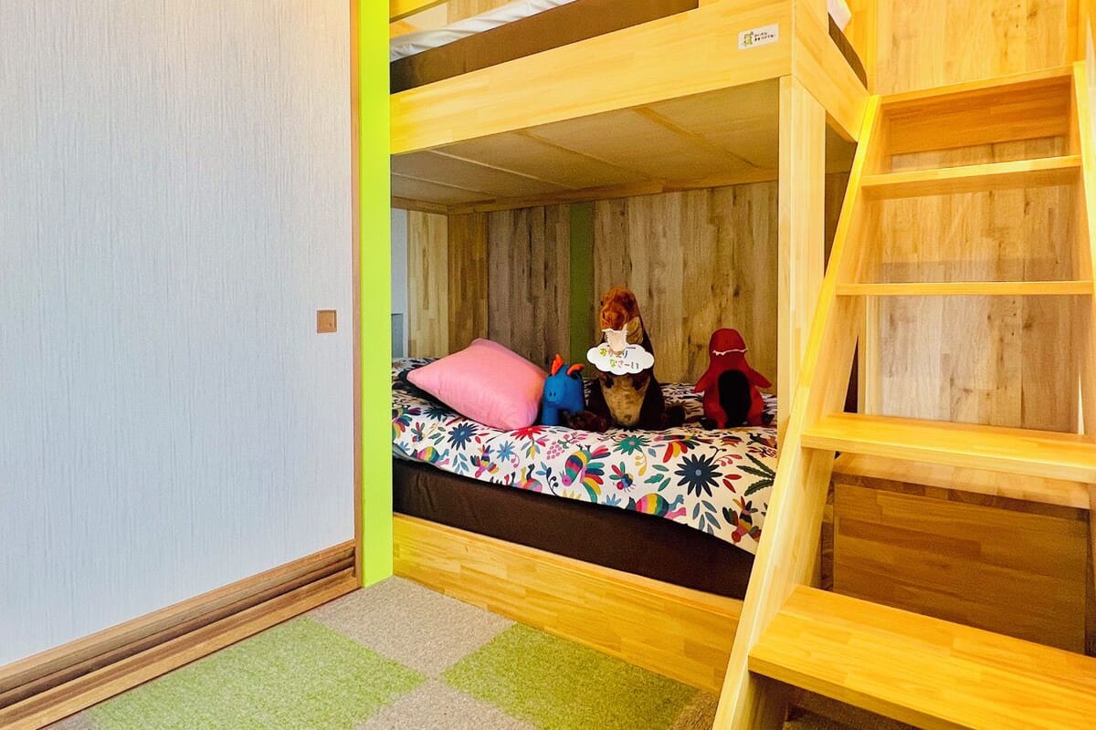 Ein Schlafraum mit Etagenbett, einer Holzleiter, einer bunten Bettdecke und einem grünen Teppich.