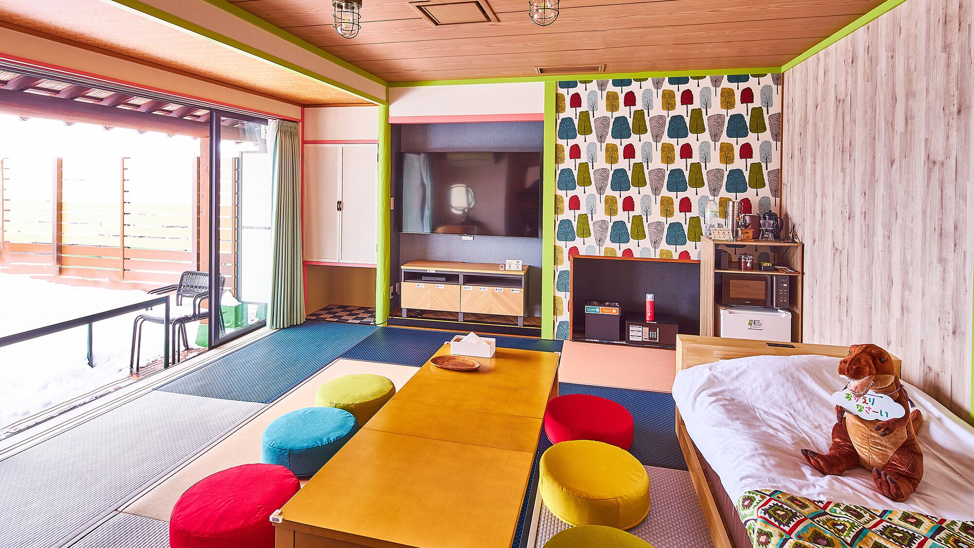 Ein Zimmer mit einem Bett, einem Tisch, bunten Kissen, einem Fernseher und einer Wand mit Muster.