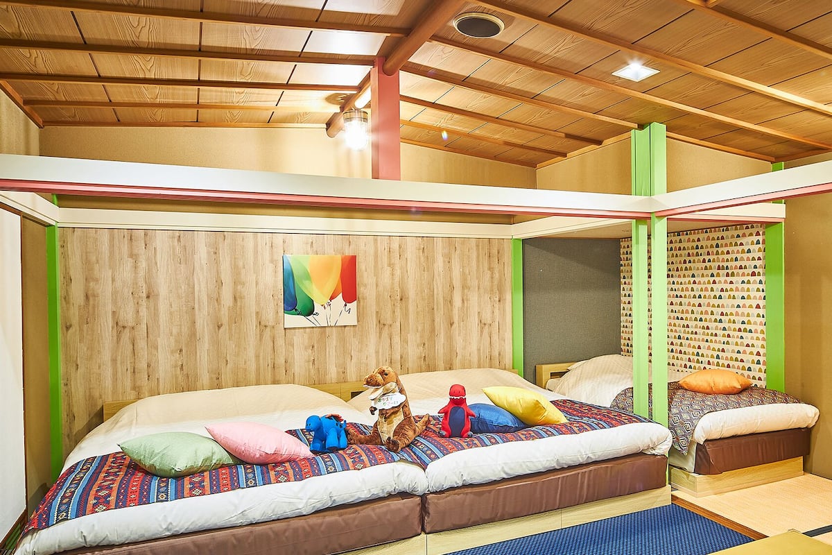 Ein Zimmer mit Holzboden, einem Bett mit bunter Bettwäsche und einer Wand mit einem gemusterten Design.