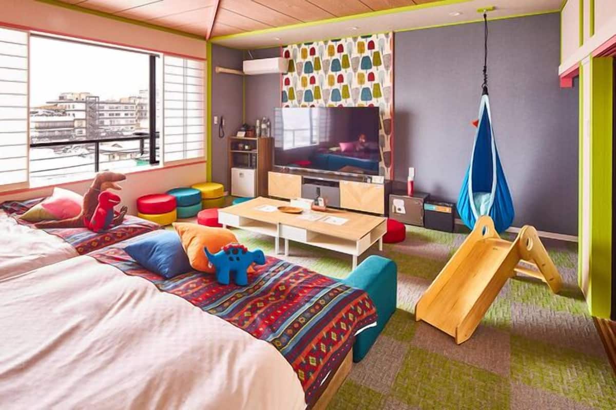 Ein Zimmer mit Bett, Fernseher, Spielbereich mit bunten Hocker und einer Hängeschaukel.