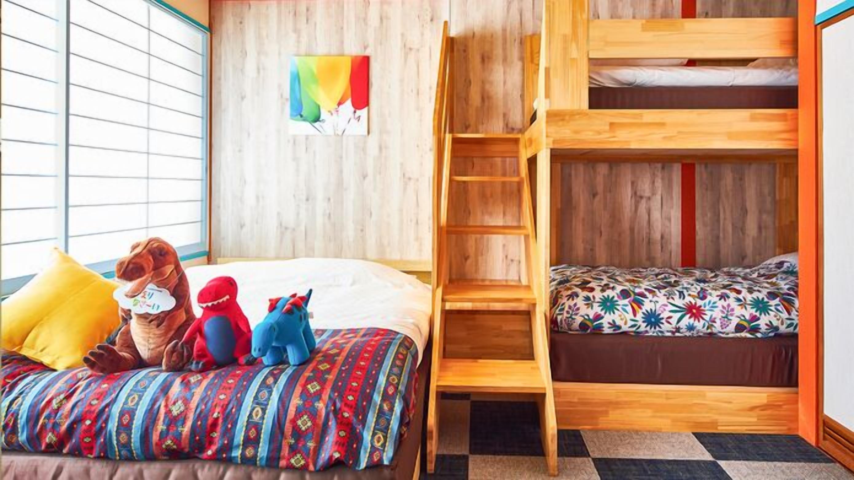 Ein Zimmer mit einem Etagenbett, einer Stehleiter, einer bunten Bettdecke und einem Fenster mit Jalousien.