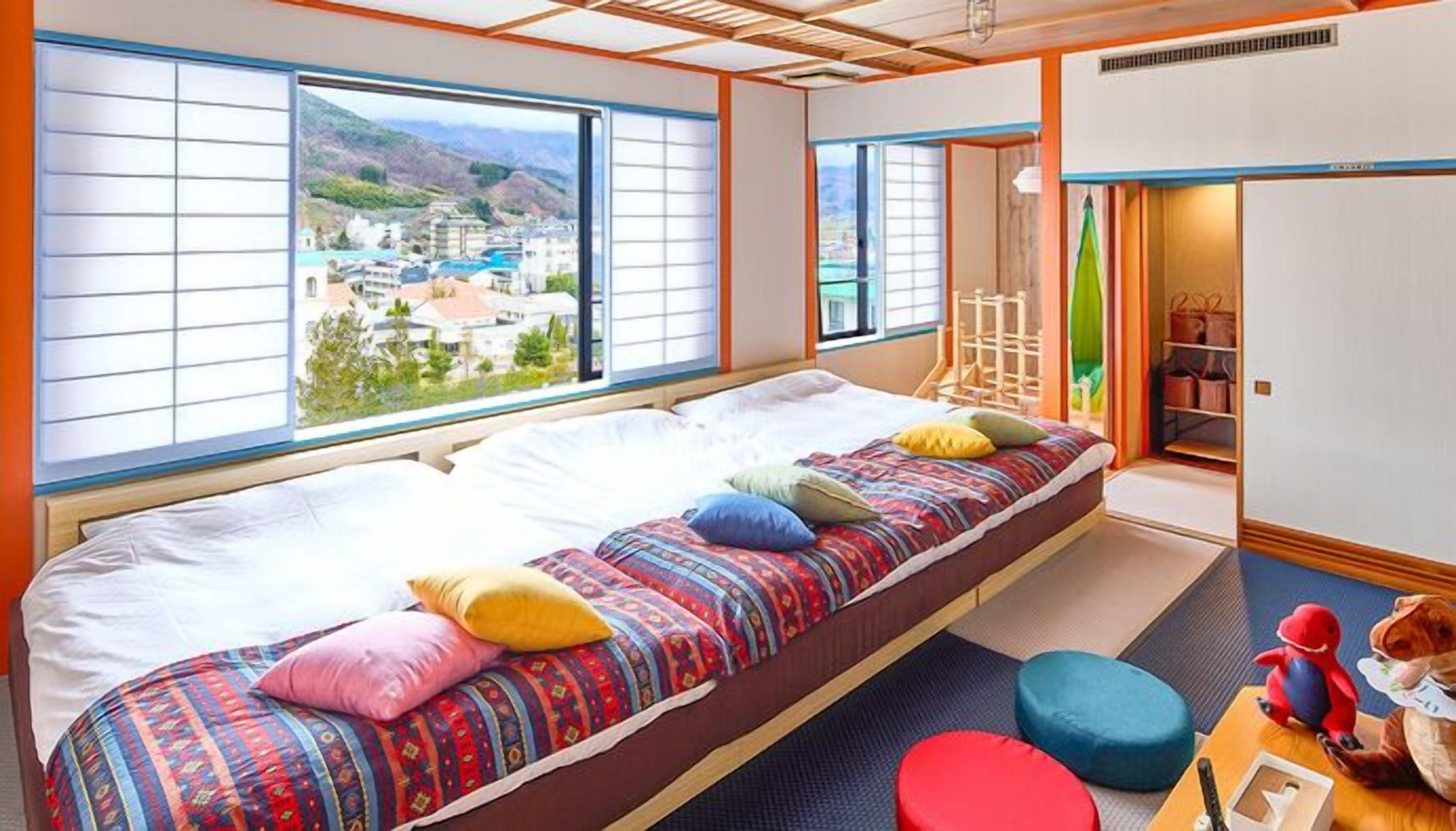 Ein Zimmer mit Bett, Blick auf eine Stadt, einem Kleiderschrank und einem kleinen Tisch mit einem Spielzeug.