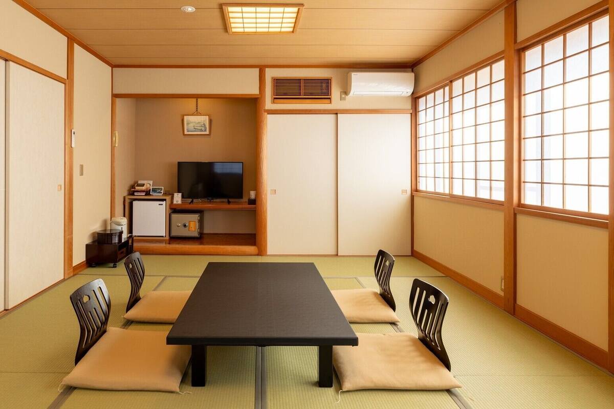 A traditional Japanese room with tatami flooring, a low table with cushions, a television, and a heater.