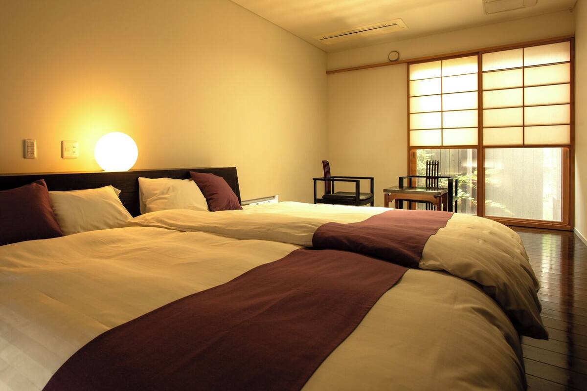 A hotel room with two beds, a sitting area with a table and chairs, and a large window with a view.