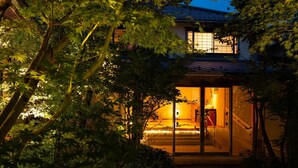 Una casa tradicional japonesa con fachada de madera, puerta de entrada corredera de vidrio y una escalera interior visible.