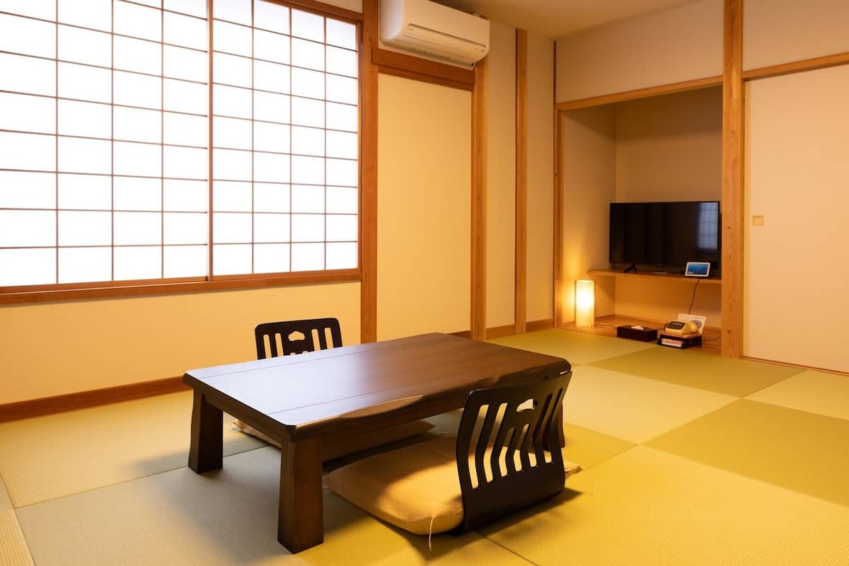 A traditional Japanese room with tatami flooring, a low table, and a television on a shelf.