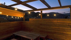 An outdoor wooden deck with benches and string lights. - Kawazu Log House (Kawazu)