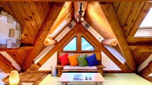 A cozy attic room with a sloped ceiling, a wooden bench with cushions, a small table, and a hanging light fixture. - Kawazu Log House (Kawazu)