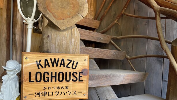 A wooden sign with 'KAWAZU LOGHOUSE' written on it, surrounded by rustic wooden elements and a small statue. - Kawazu Log House (Kawazu)