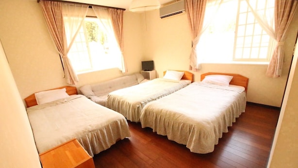 A room with two beds, wooden flooring, a nightstand, and a window with curtains. - Pension Tama House (Yuzawa)