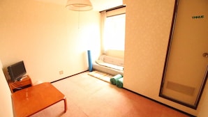 A room with a bed, a small table, a television, and a window with curtains. - Pension Tama House (Yuzawa)