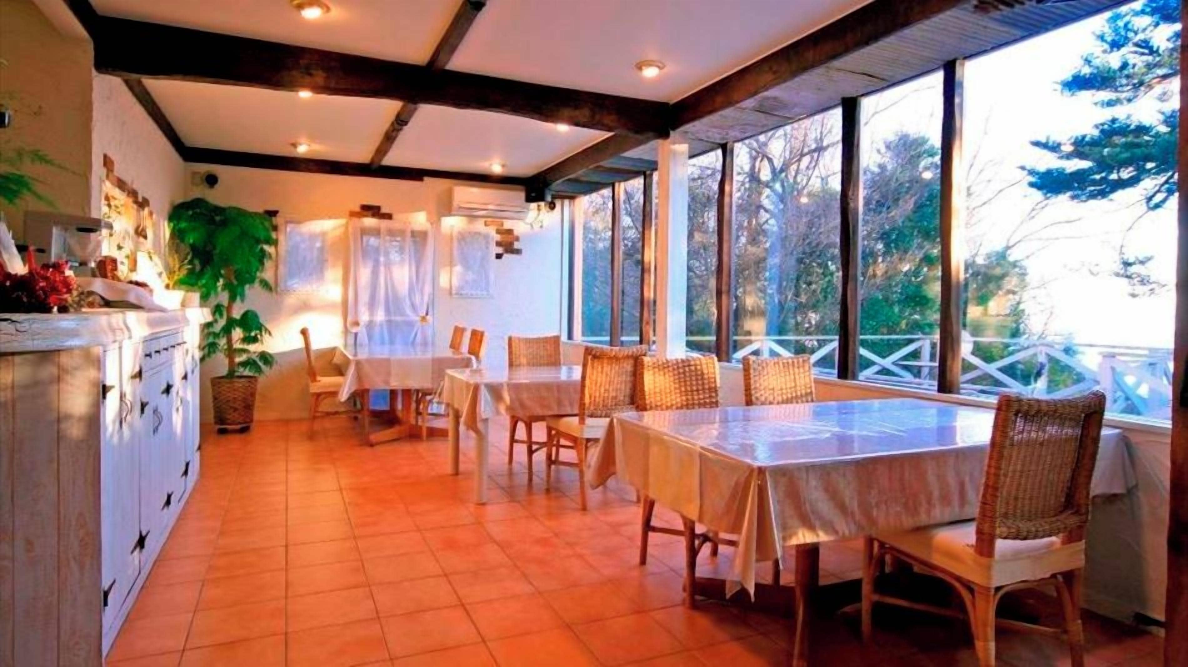 Un comedor con mesas y sillas, ventanas amplias y vista a árboles.