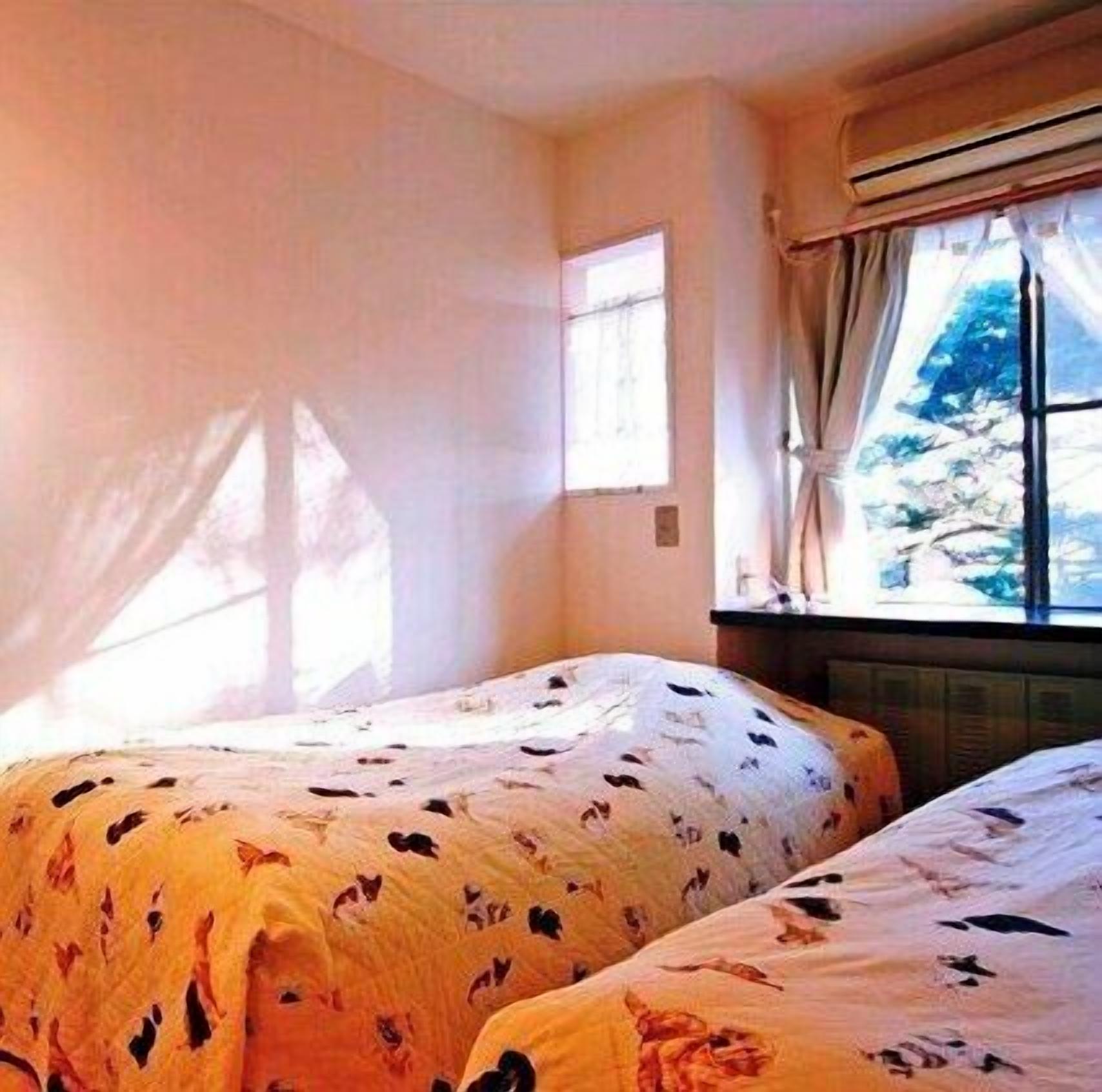 A room with two beds, a window with curtains, and a wall-mounted air conditioning unit.