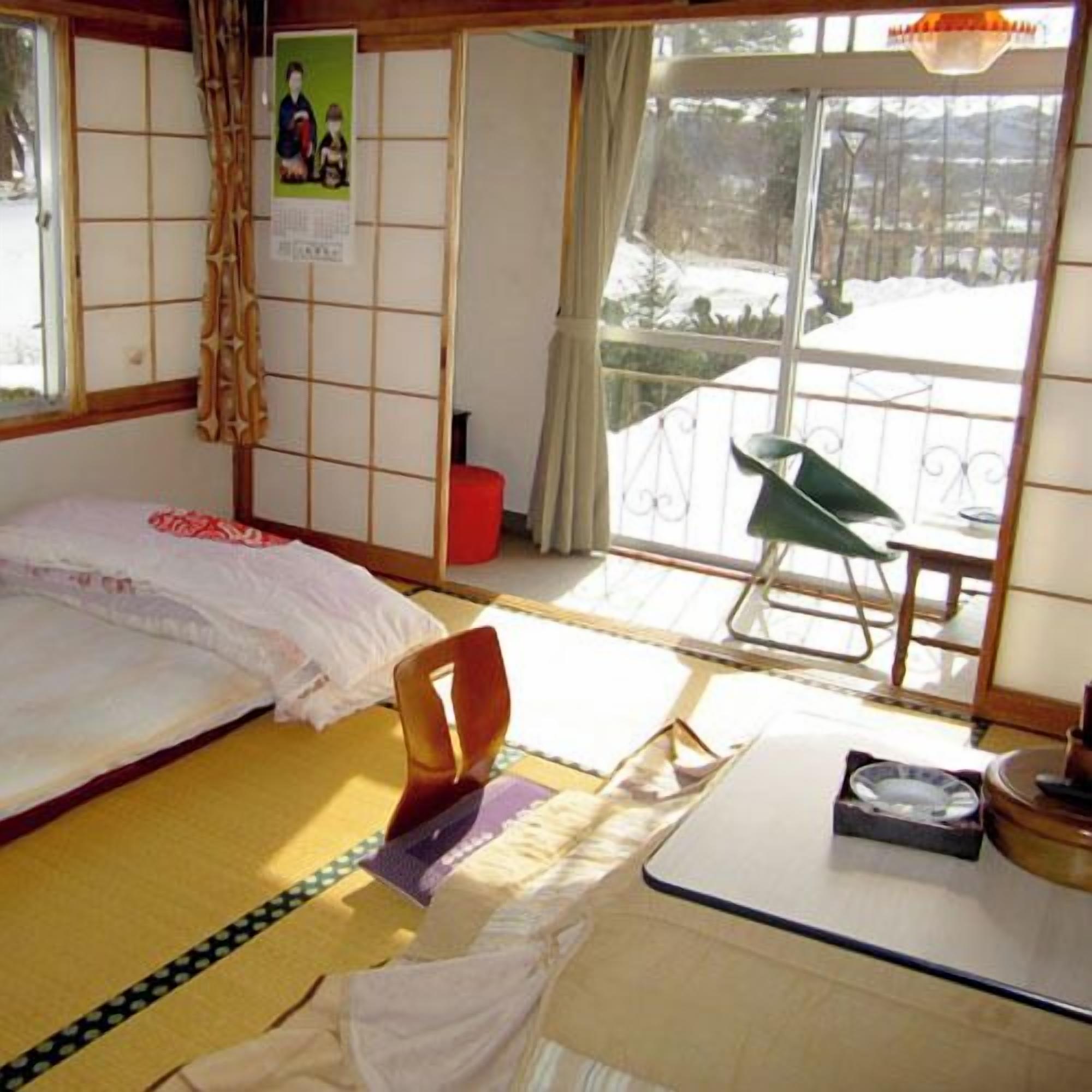 Une pièce de style japonais traditionnel, avec un sol recouvert de tatamis, un futon servant de lit, une petite table basse et une porte coulissante donnant sur un balcon.