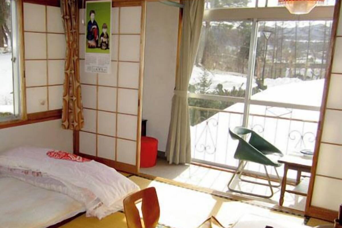 Ein traditioneller japanischer Raum mit Tatami-Bodenbelag, einem Futon, einem niedrigen Tisch und einer Schiebetür, die auf einen Balkon führt.
