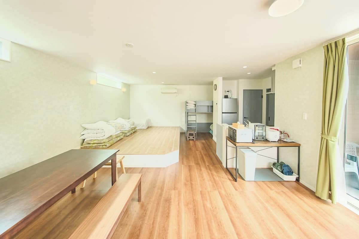 Ein modernes Hotelzimmer mit Holzboden, einem Bett mit weißen Leinentextilien, einem kleinen Schreibtisch mit Computer und einem Fenster mit Vorhängen.