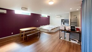 A compact room with a bed, a small table, a bench, a kitchenette, and a window. - Chokotto Villa Maestro (Sumoto)