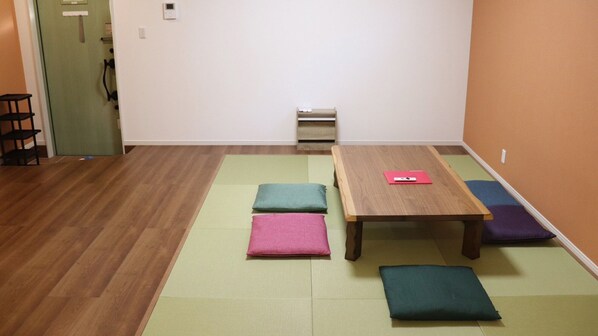A room with a wooden table, colorful cushions, a small shelf, and a door. - Chokotto Villa Maestro (Sumoto)