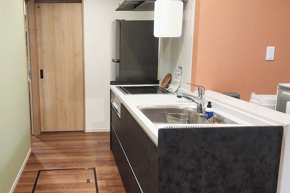 A kitchen with a wooden door, a black refrigerator, a white sink, and a stainless steel faucet.