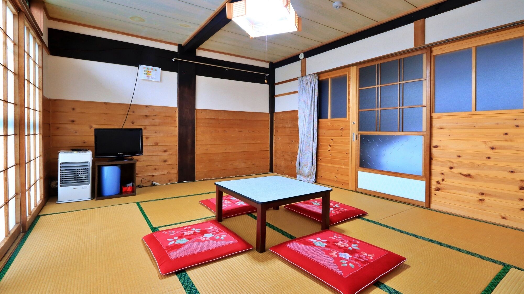 Egy tatami szőnyegekkel borított szoba, alacsony asztallal és párnákkal, egy televízióval és egy fűtőberendezéssel.