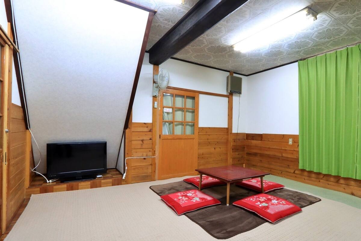 Une pièce avec un plancher en bois, un tatami, une petite table et un rideau vert.