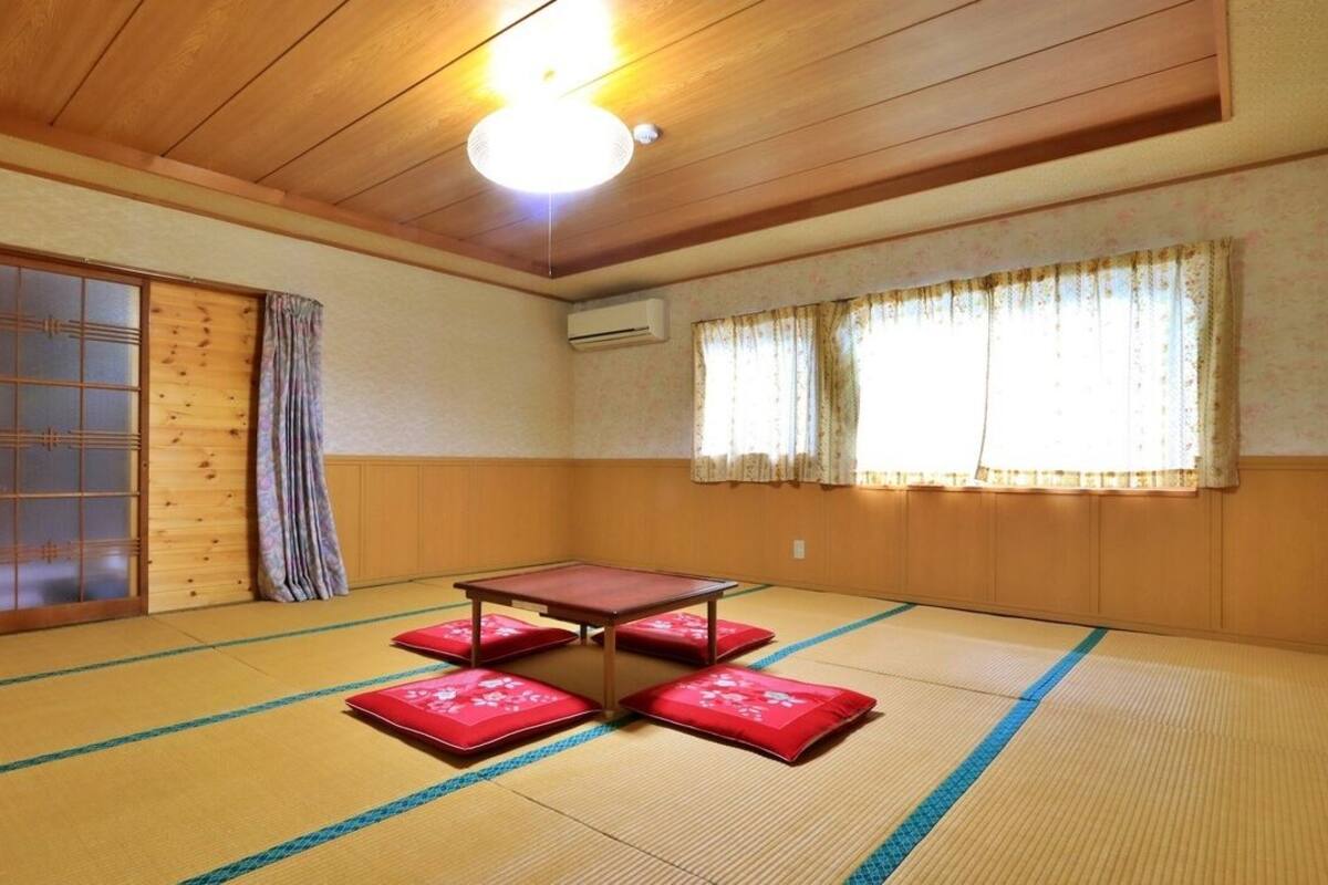 Une pièce avec un sol recouvert de tatamis, une porte coulissante, une table avec des coussins et un luminaire au plafond.