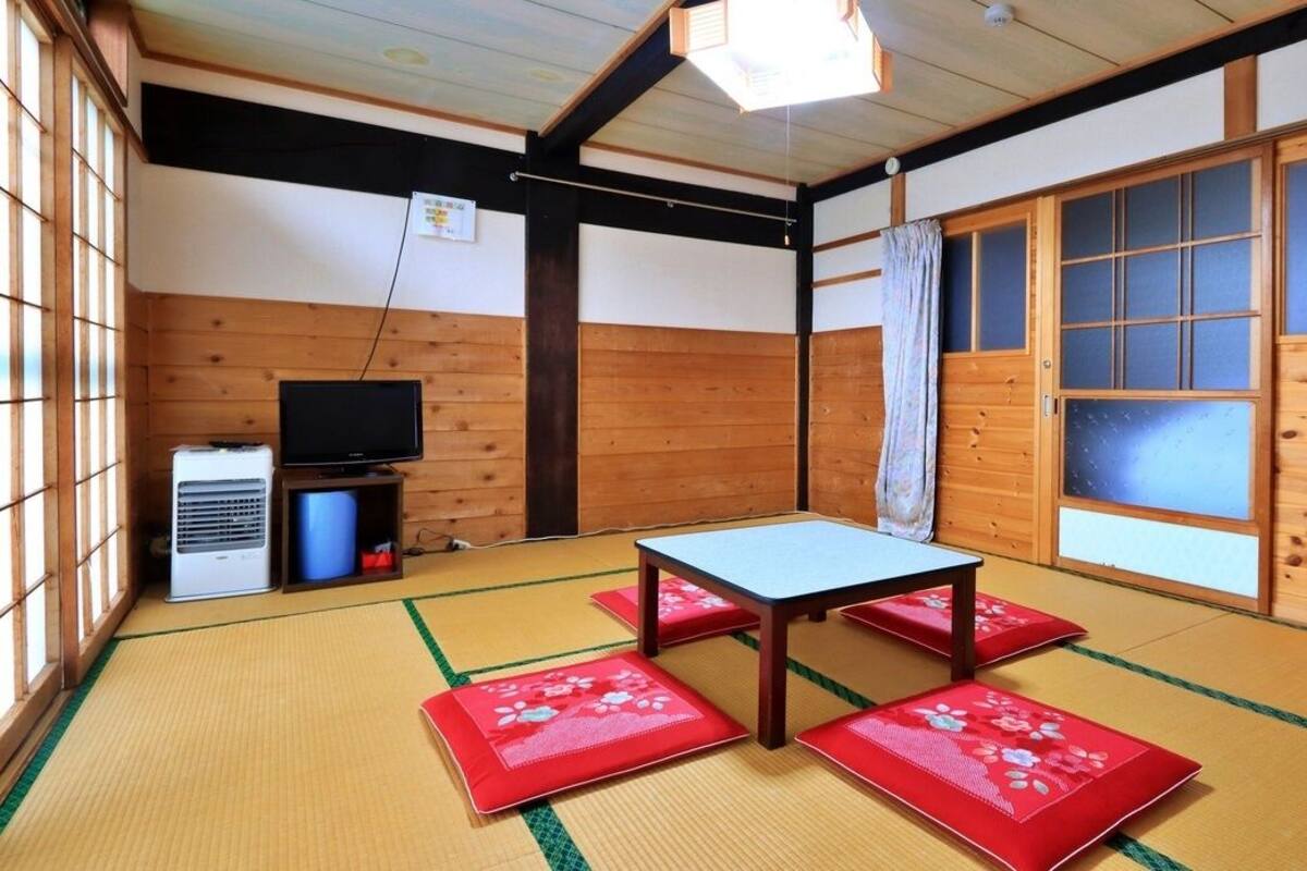 Une pièce avec un sol recouvert de tatamis, une table, un téléviseur et un radiateur.