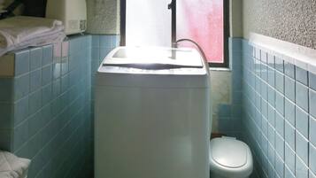 A compact bathroom with a white washing machine, a toilet, and blue tiled walls.