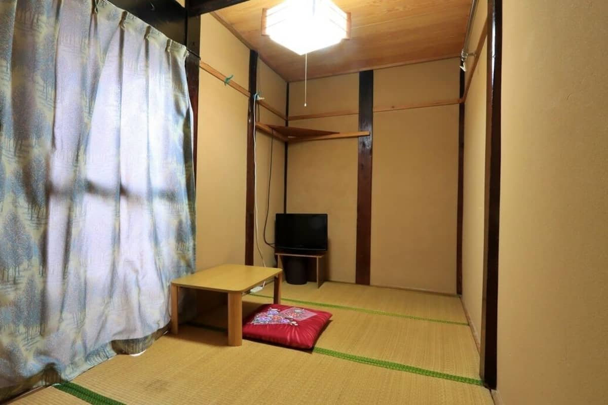 Une pièce avec un sol recouvert de tatamis, une petite table, un téléviseur et un rideau.