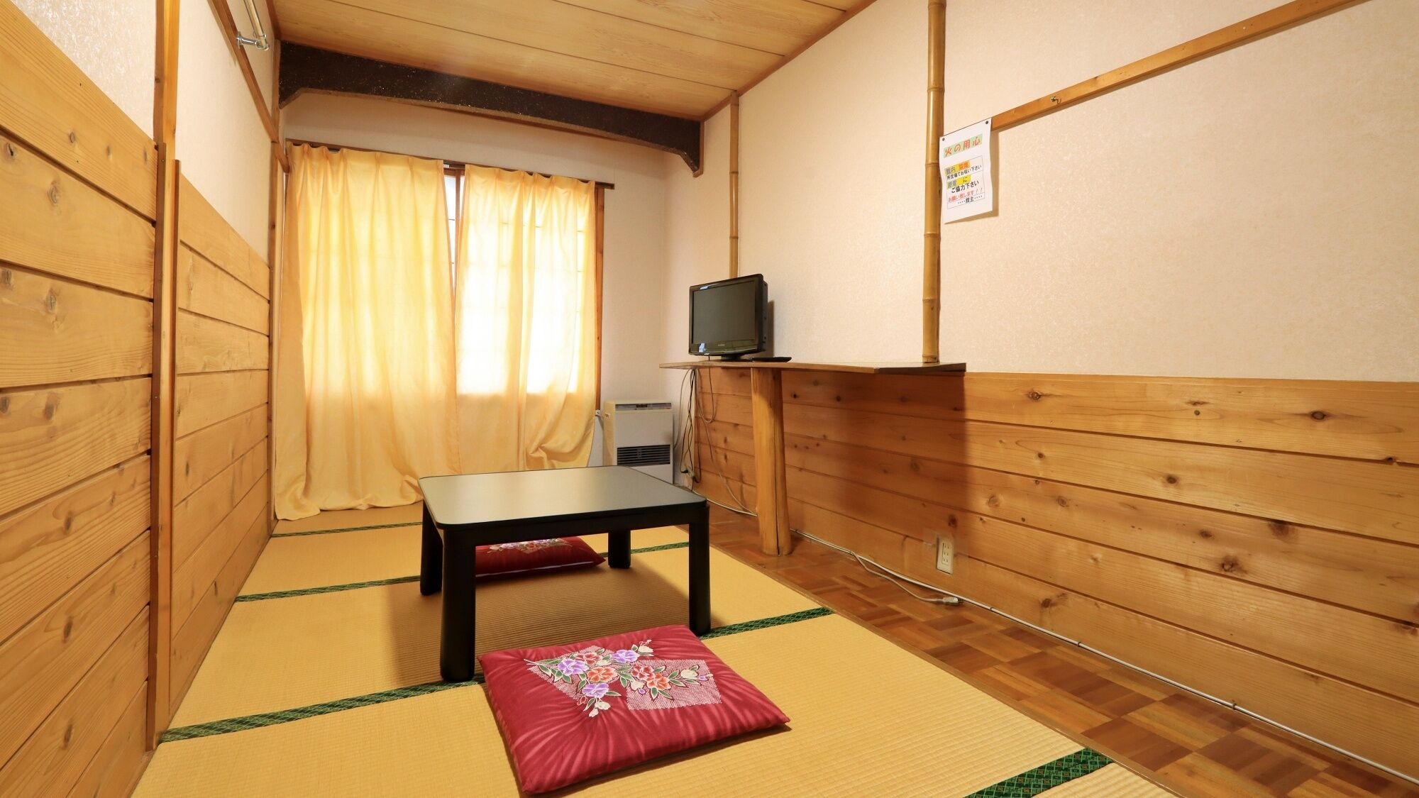 Egy hagyományos japán szoba, tatamiszőnyeggel borított padlóval, alacsony asztallal, egy faállványon elhelyezett televízióval és függönnyel ellátott, tolóajtóval.