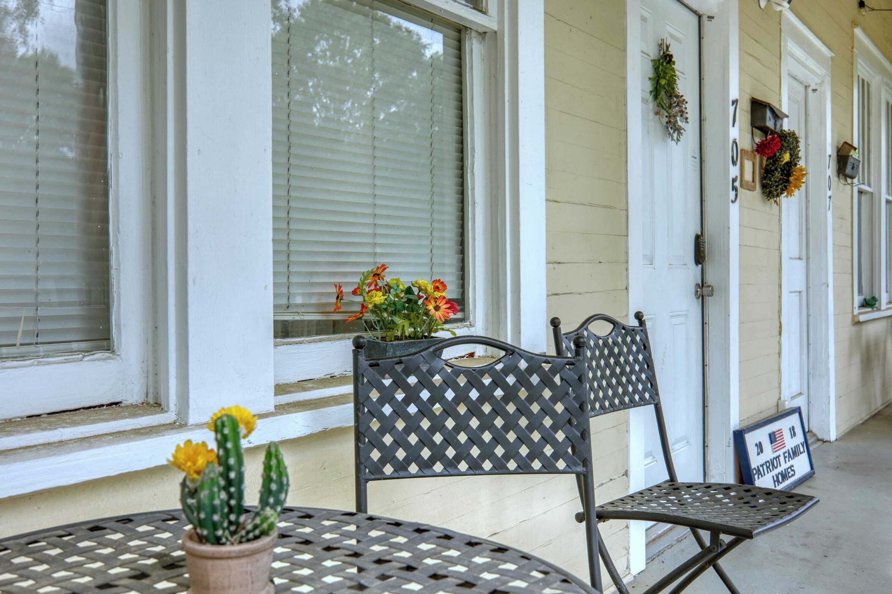 Eine Veranda mit einem Metalltisch und -stühlen, einem Blumentopf mit Blumen sowie einem Schild mit der Aufschrift 'Patriot Family Homes'.