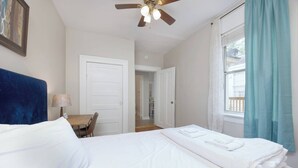 A hotel room with a bed, a ceiling fan, a desk with a chair, and a window with curtains. - Near Chattahoochee River & Shops - Central Duplex (Columbus)