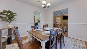 A dining room with a wooden table, chairs, a chandelier, and a potted plant.