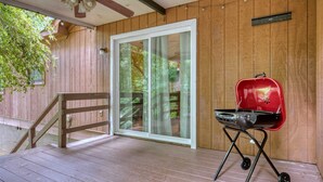 A wooden deck with a sliding glass door, a red grill, and a ceiling fan.