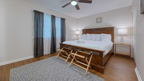 A bedroom with a bed, a ceiling fan, two bedside lamps, a wooden headboard, and a window with curtains.