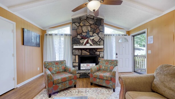 A living room with a stone fireplace, two floral armchairs, a sofa, and a ceiling fan.