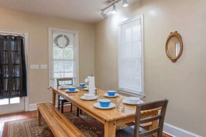 A dining room with a wooden table set for four, a bench, and a mirror on the wall. - Downtown, Moments from Riverwalk-Broadway Bungalow (Columbus)