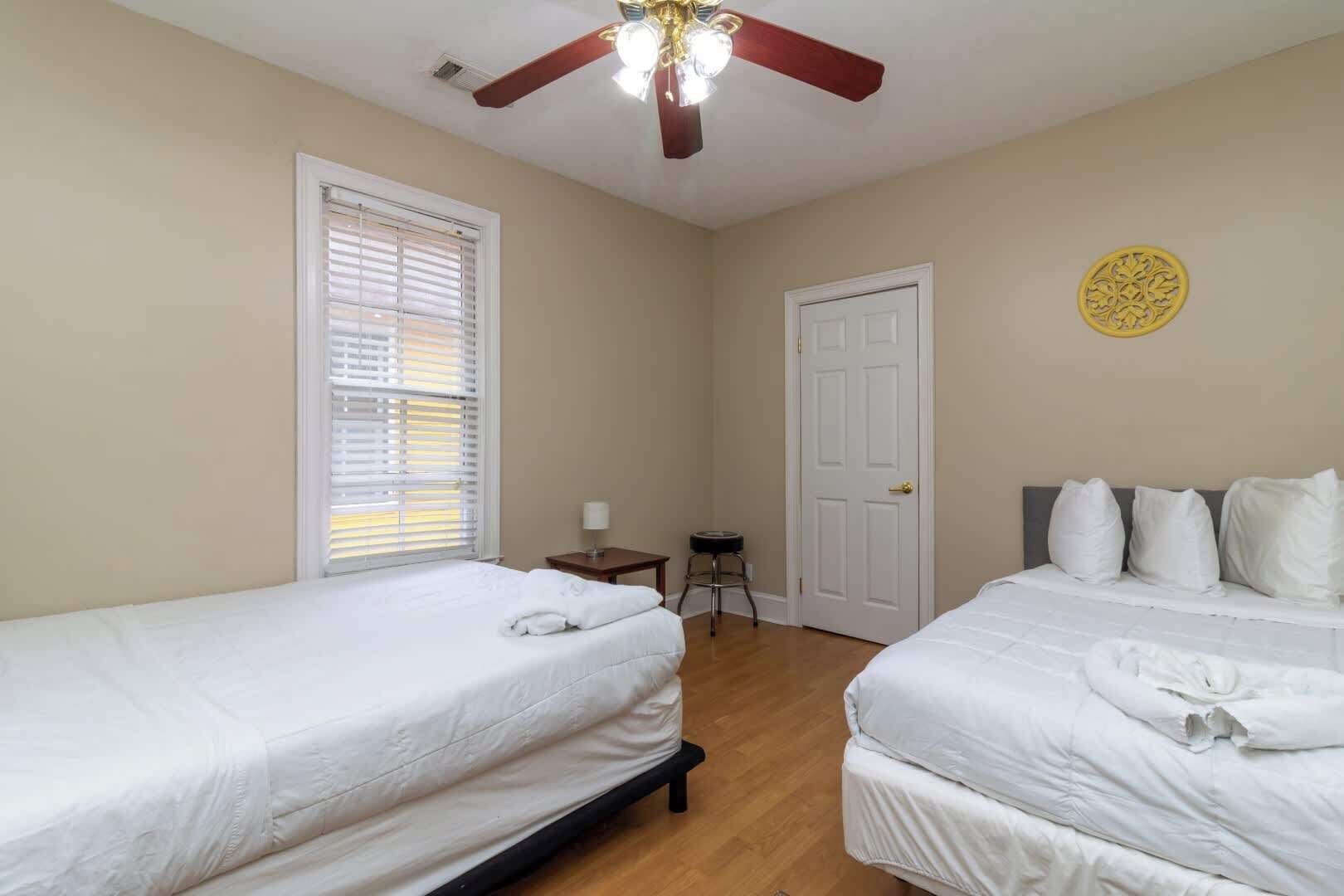 A bedroom with two single beds, a ceiling fan, a door, and a small table with a lamp.
