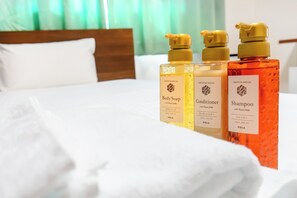 A bed with white linens and three bottles of shower products on it. - Imari Liberty Hotel (Imari)