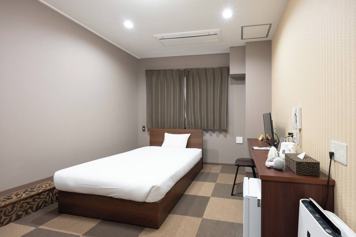 A hotel room with a bed, a desk with a computer, a chair, and a television.