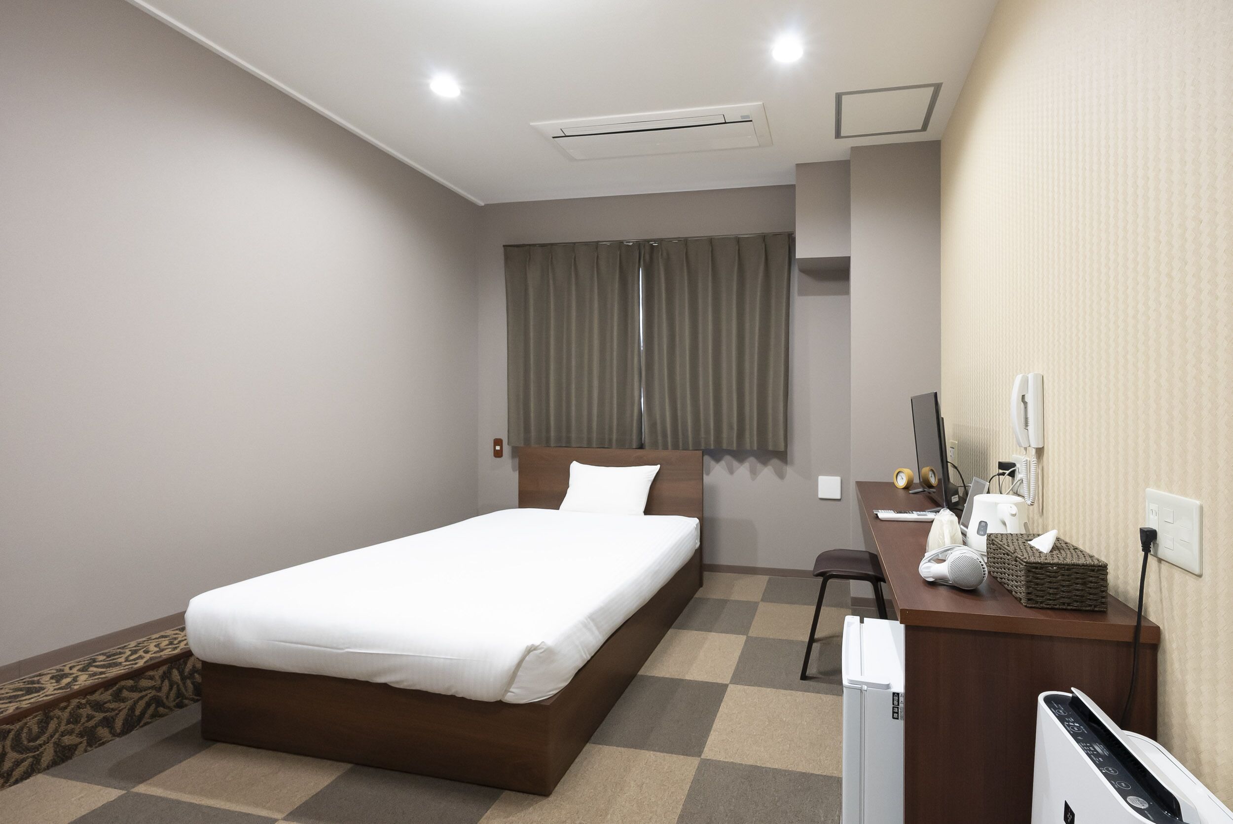 A hotel room with a bed, a desk with a computer, a chair, a TV, and a window with curtains.