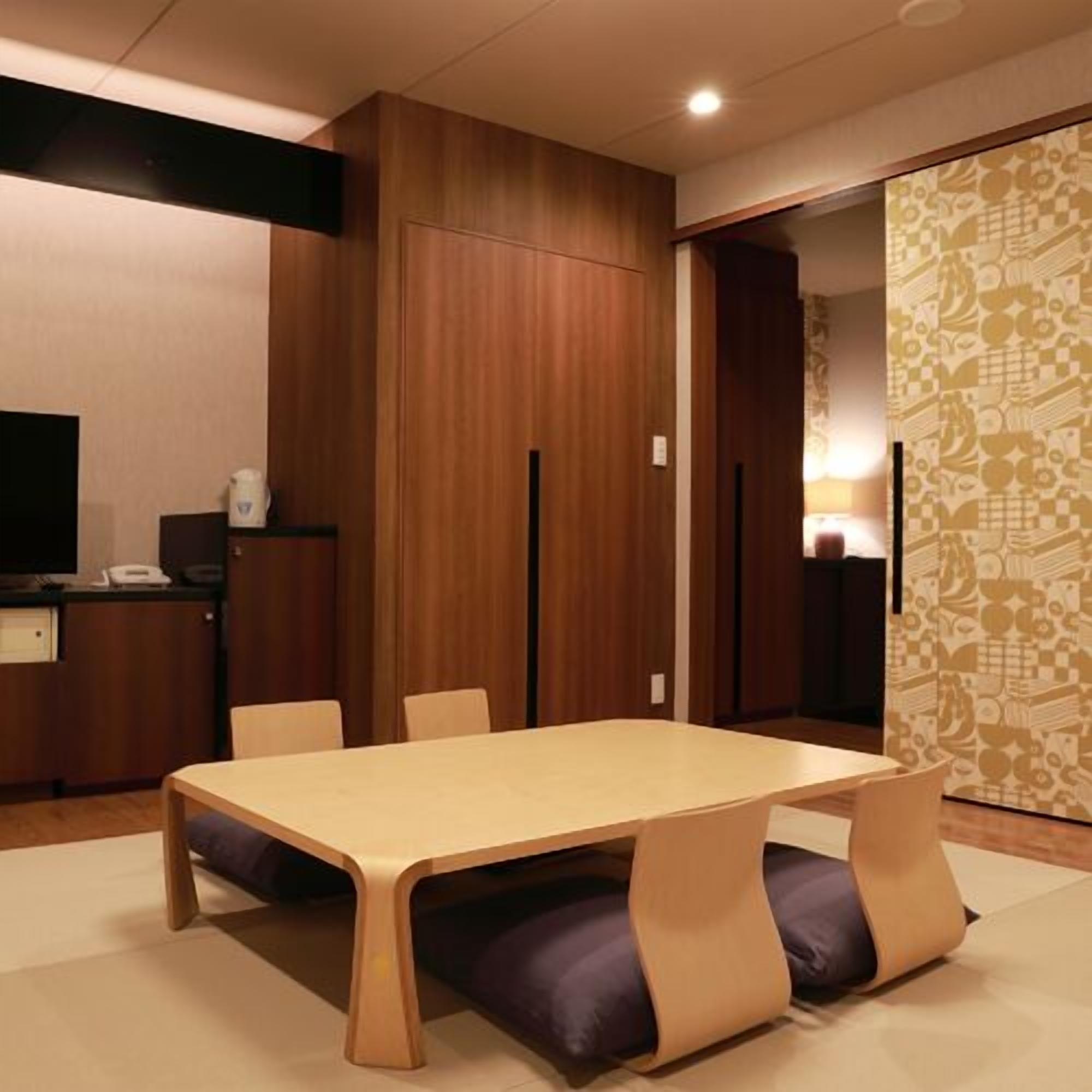 Une chambre moderne avec une table en bois, des chaises, un téléviseur et un mur orné d’un motif.