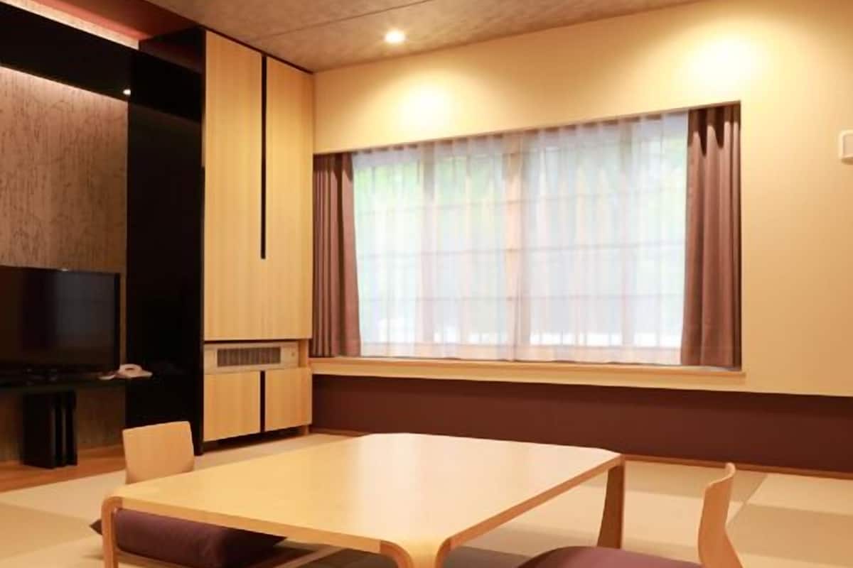 Ein modernes Zimmer mit einem großen Tisch, Stühlen, einem Fernseher und einem Fenster mit Vorhängen.