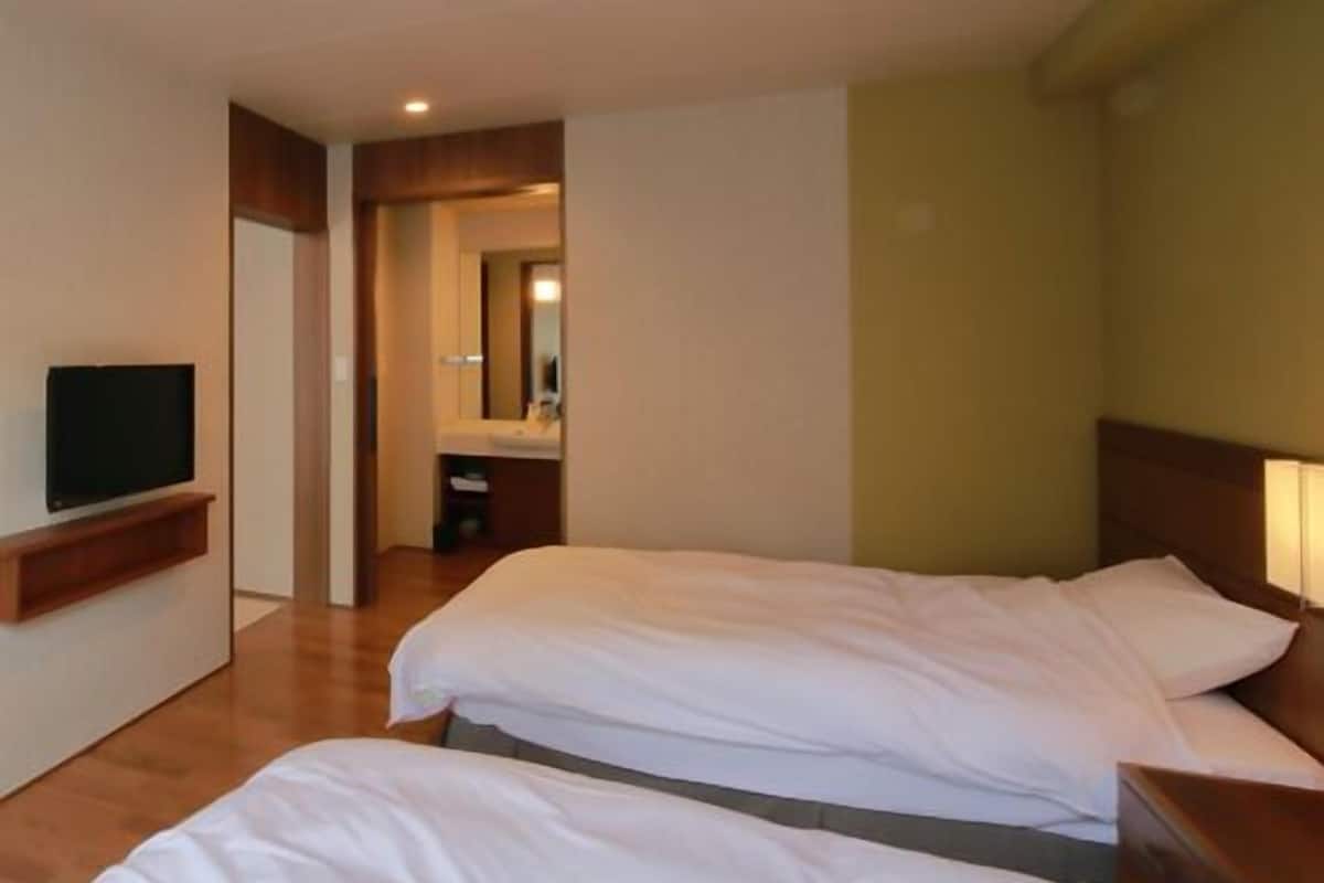 Ein Hotelzimmer mit zwei Betten, einem Fernseher, einem Spiegel und einem durchgehenden Türspalt sichtbaren Badezimmer.